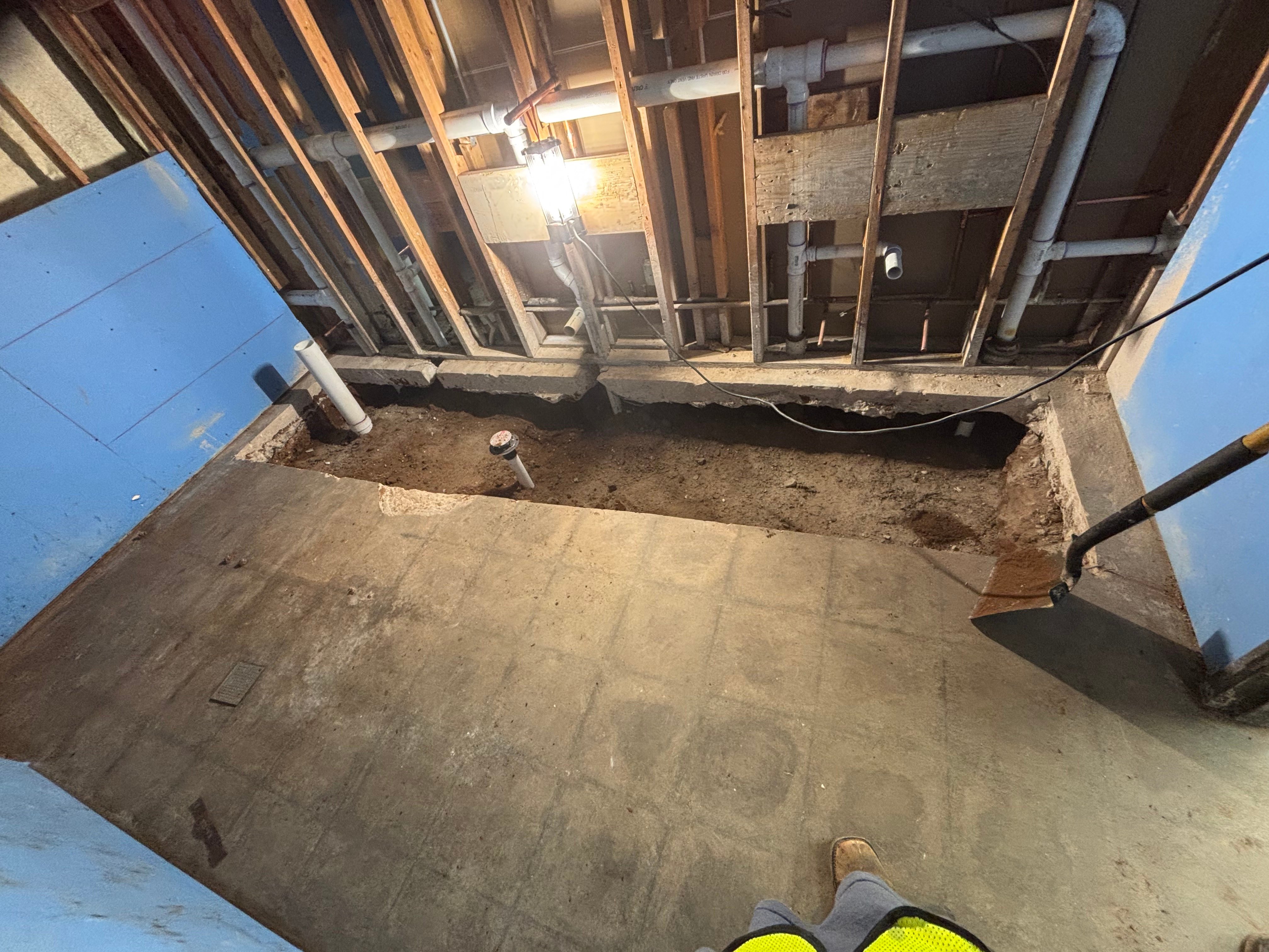 Underground plumbing installation with PVC pipes and metal fittings in excavated foundation area