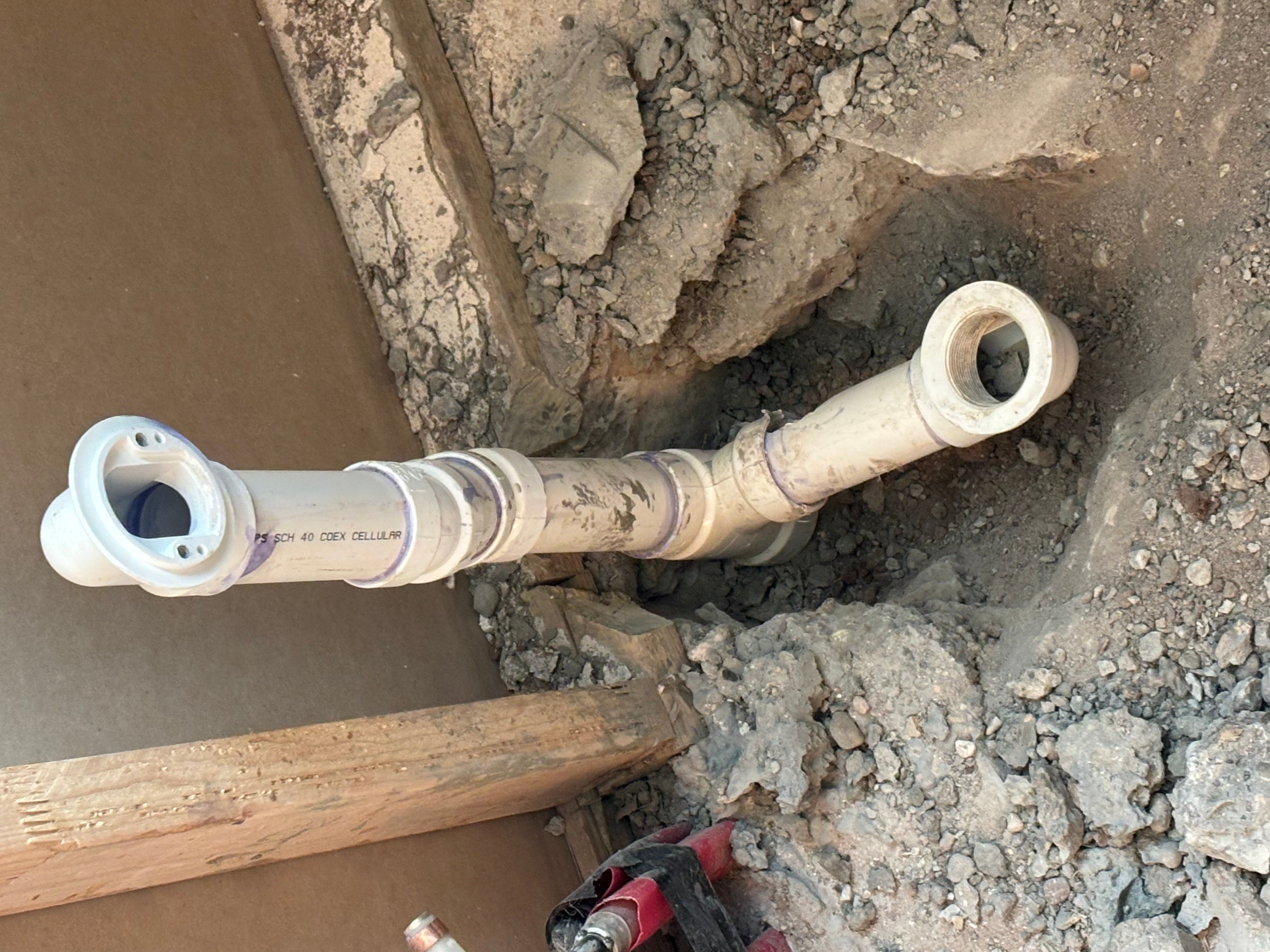 PVC drain pipe with white couplings installed in excavated trench with soil backfill