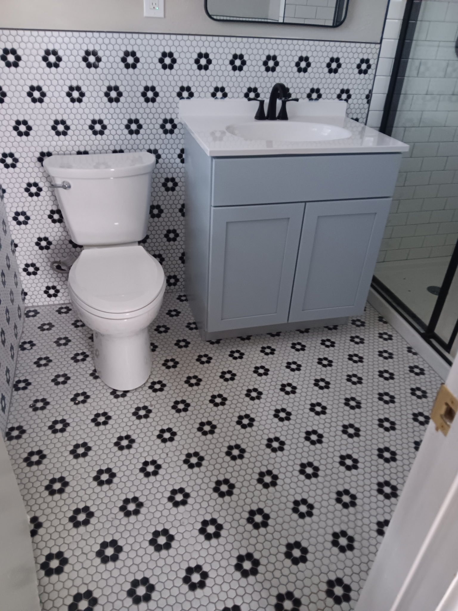 Newly renovated bathroom with white hexagonal tile flooring, black flower pattern, gray vanity, and white toilet