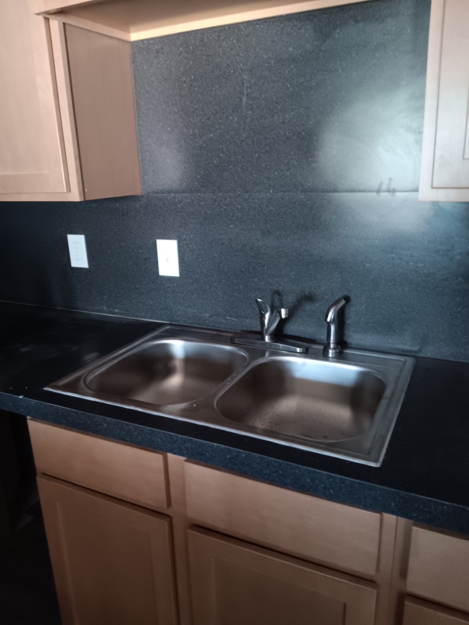 Dual-basin stainless steel kitchen sink with chrome faucet on dark granite countertop