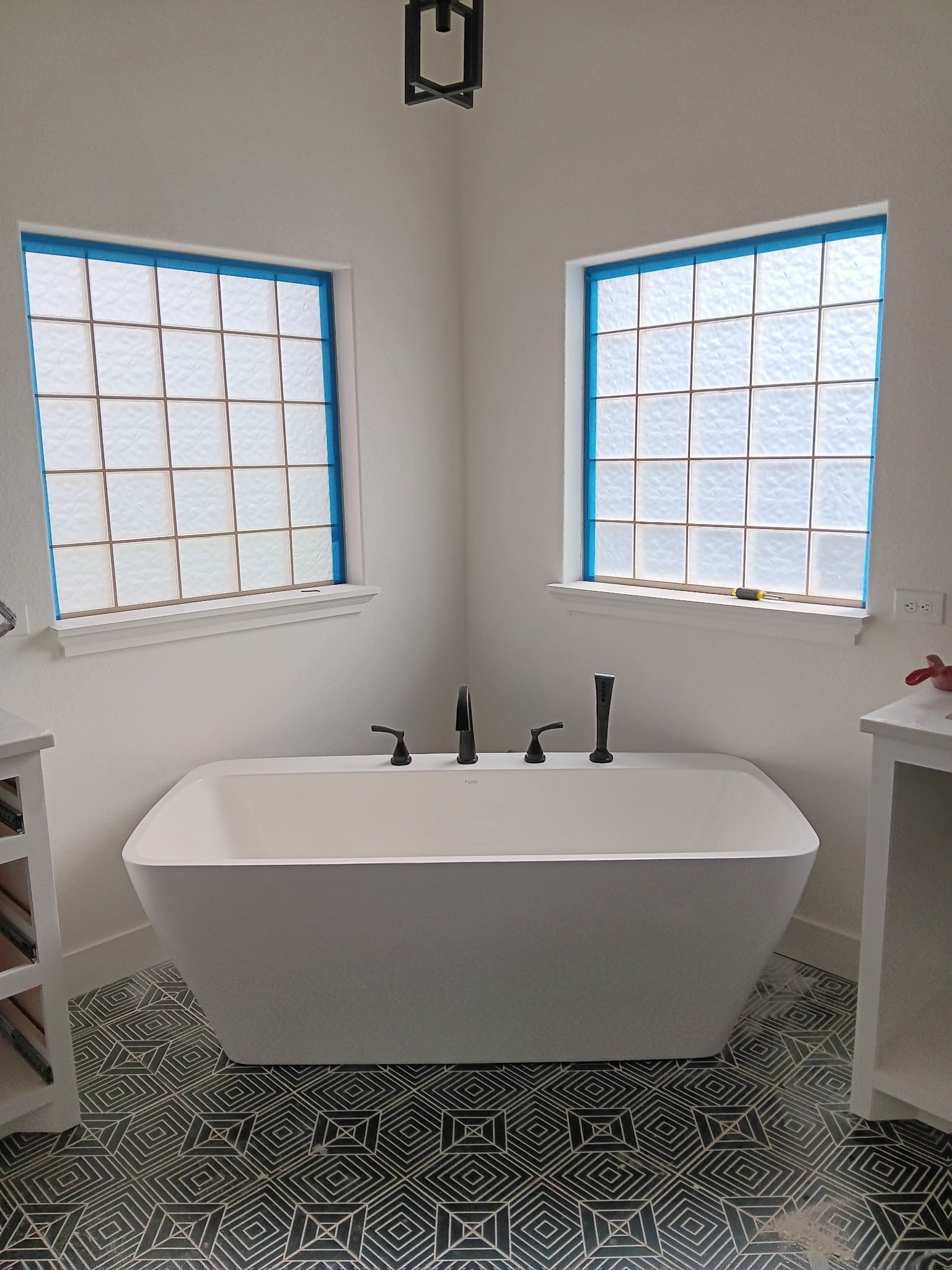 White freestanding soaking tub with black fixtures in bright bathroom with geometric tile floor